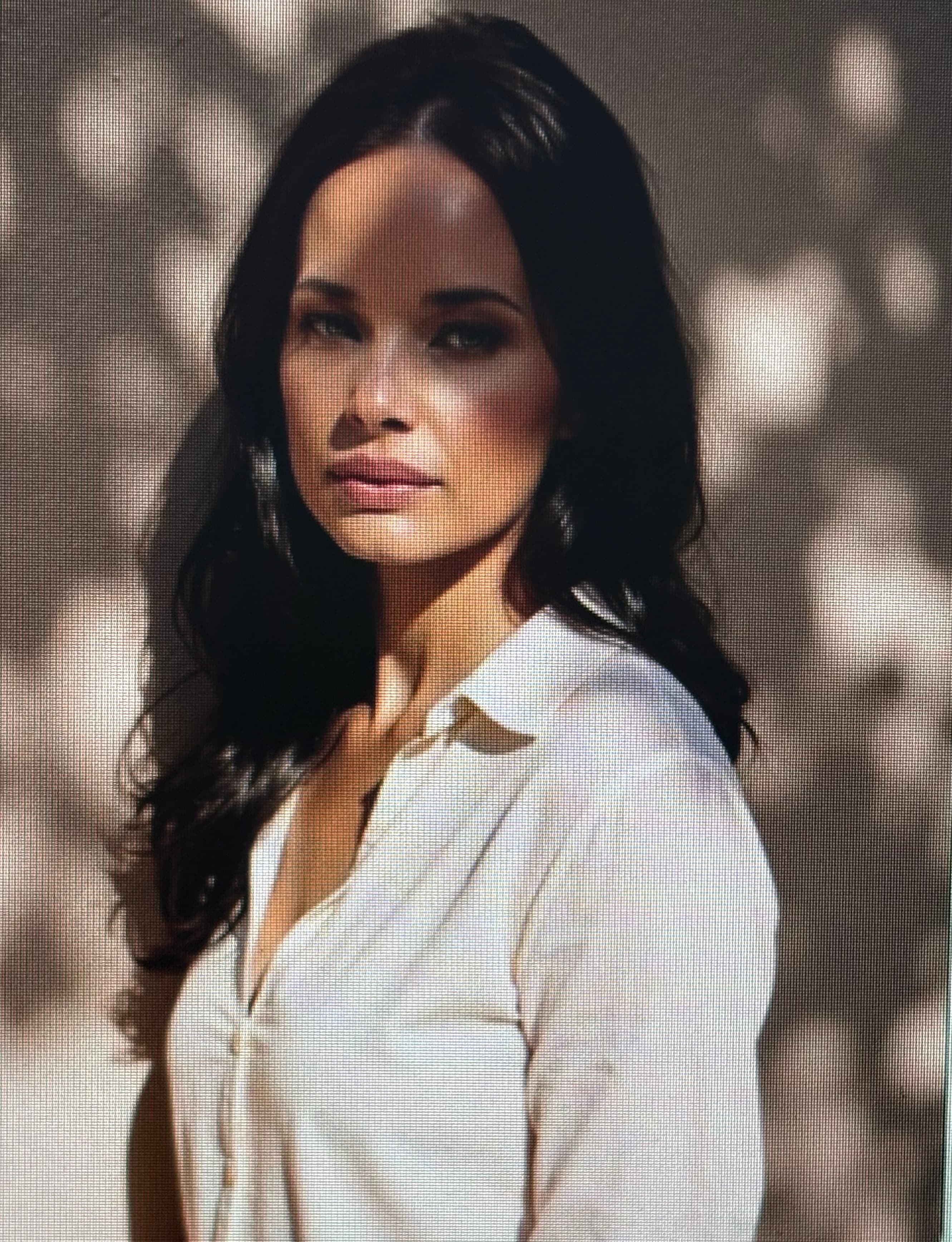 Woman with long dark hair in a white shirt, illuminated by soft, dappled sunlight shadows.