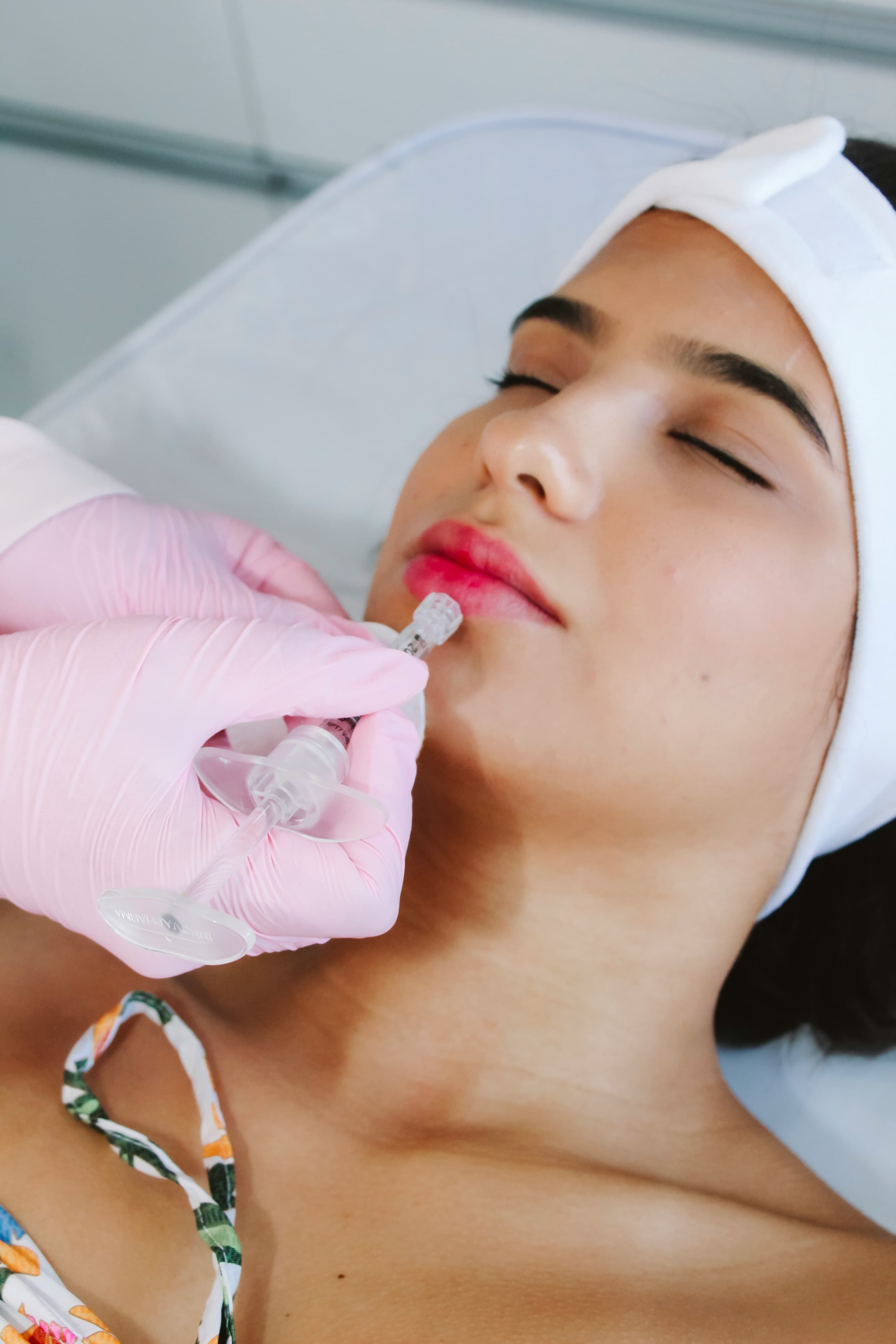 Close-up of a woman receiving a lip filler injection from a professional wearing pink gloves.
