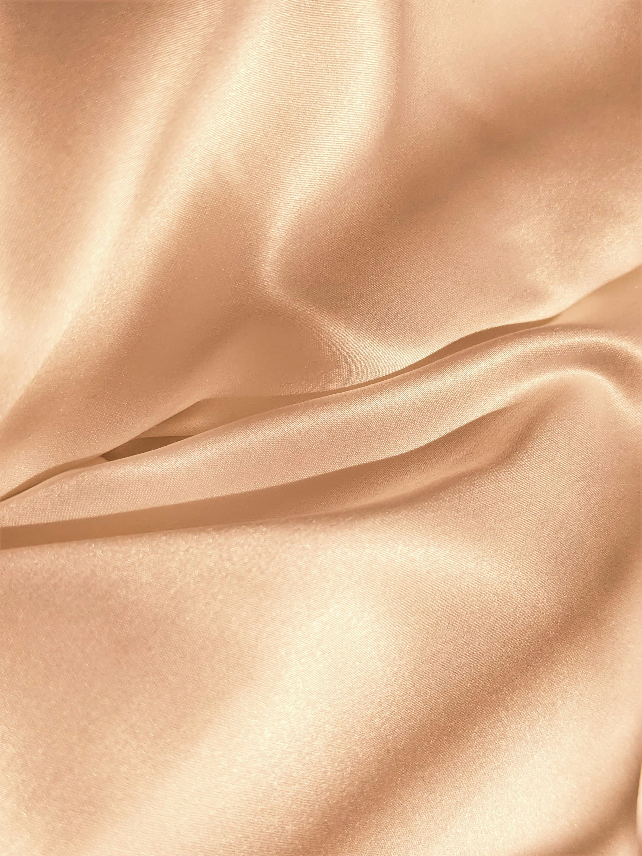Shimmering champagne-colored silk fabric with soft, elegant folds and a smooth, lustrous texture.